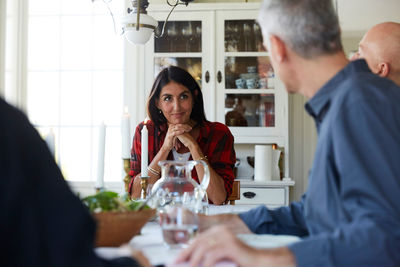 Smiling mature woman looking at male friends while sitting in dining room