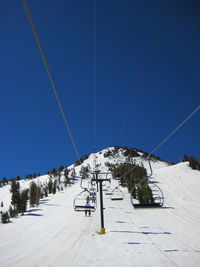 Ski lift over snowcapped mountains against blue sky