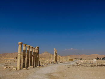 Rear view of man standing on desert against clear blue sky