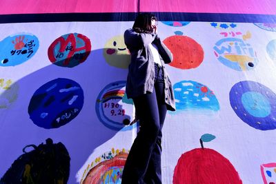 Rear view of woman standing against graffiti wall