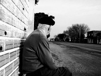 Side view of young man sitting against wall