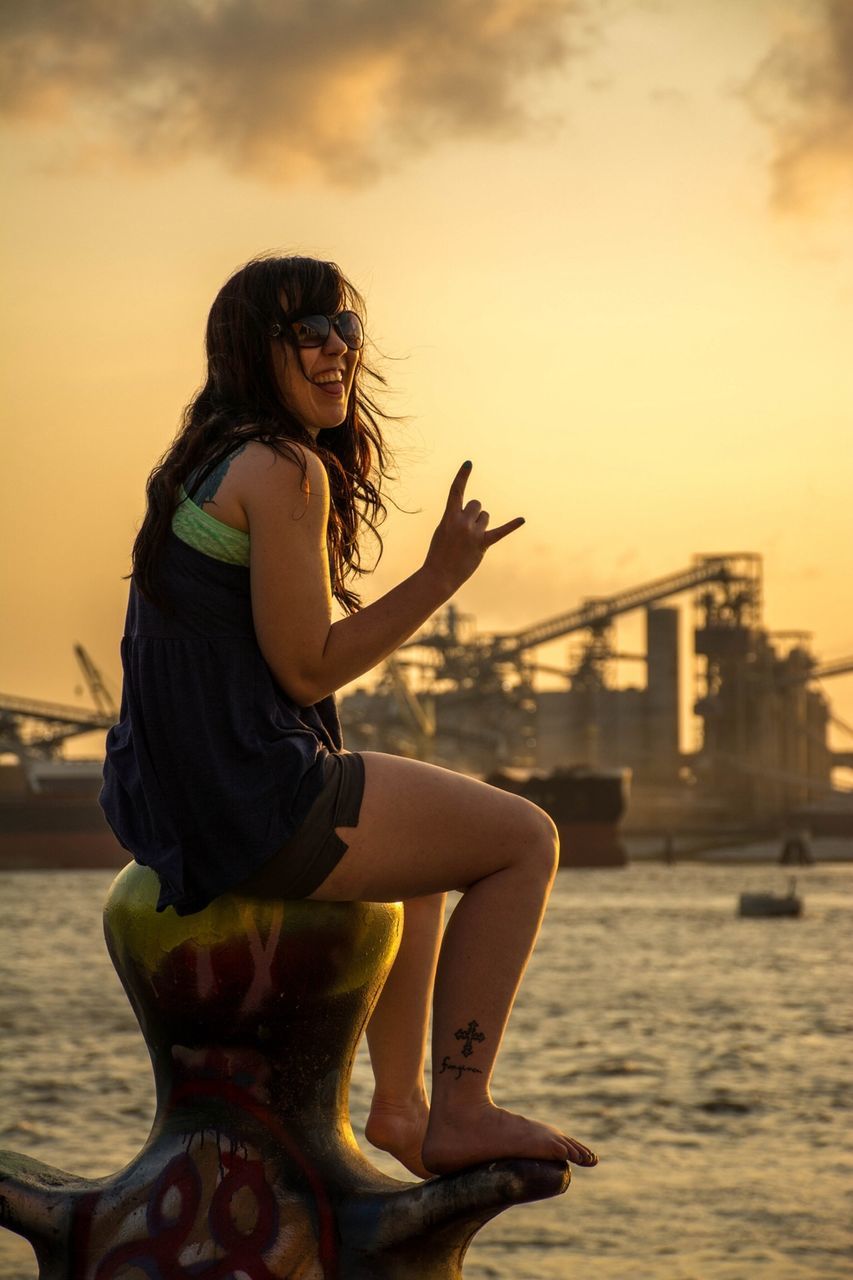 young adult, lifestyles, person, young women, leisure activity, sky, water, casual clothing, sunset, three quarter length, standing, sunglasses, looking at camera, portrait, full length, side view, focus on foreground