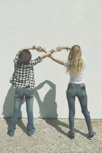 Rear view of female friends holding hands against wall