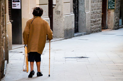 Rear view of pensioner walking on street in city