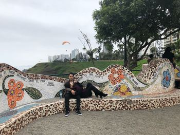 Young couple sitting on tree against sky