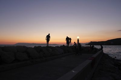 Silhouette people at beach against sky during sunset