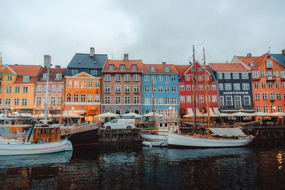 Boats moored in canal amidst buildings in city against sky