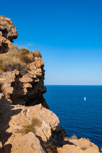 Rock formation in sea against clear blue sky