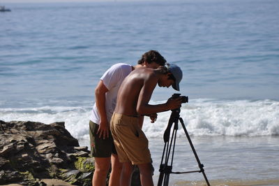 Rear view of man photographing while standing on rock at sea shore