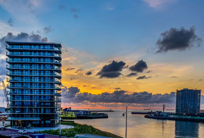 Modern building by sea against sky during sunset