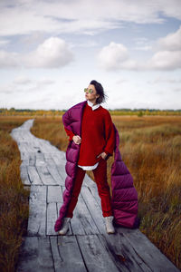 Woman  in red warm clothes and a big scarf on an ecological trail in the autumn not a swamp