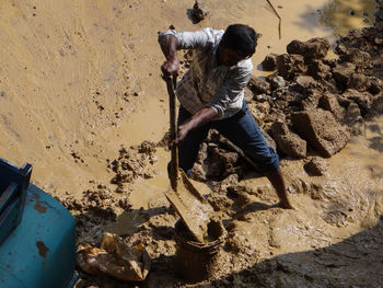 High angle view of worker digging muddy field