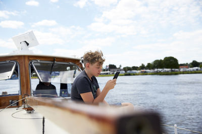 Boy using smart phone sitting on boat deck