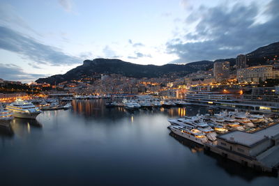 Sailboats moored on river by illuminated buildings in city against sky