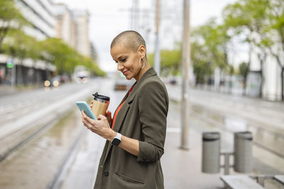 Woman using smart phone waiting at tram station platform