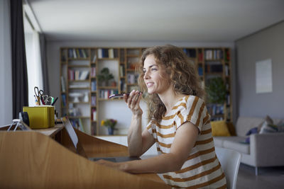 Woman talking on mobile phone while sitting by desk at home
