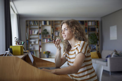 Woman talking on mobile phone while sitting by desk at home