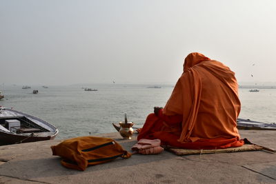 Rear view of men sitting on shore against sky