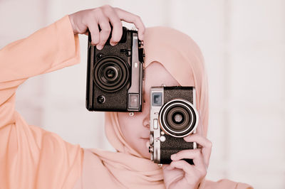 Close-up of teenage girl holding cameras against face