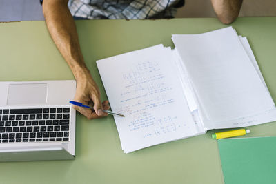 Teacher checking math paper by laptop in classroom