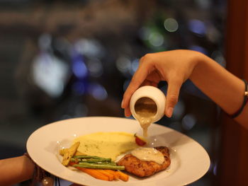 Cropped hand of person pouring sauce in meal