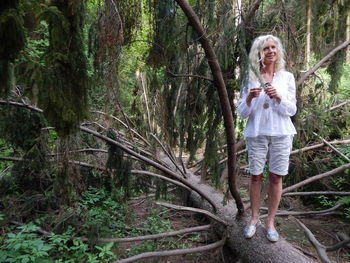 Woman standing on fallen tree trunk in forest