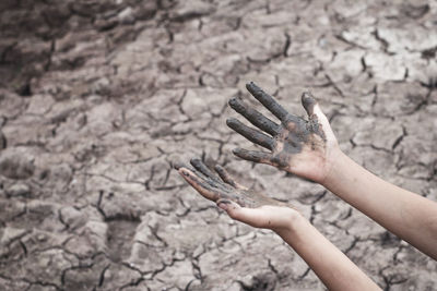 Cropped image of dirty hands over cracked field
