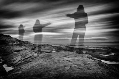 Digital composite image of man standing on rock by sea against sky