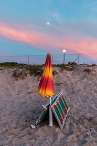 Deck chairs on beach against sky during sunset