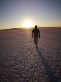 Rear view of man on beach against sky during sunset