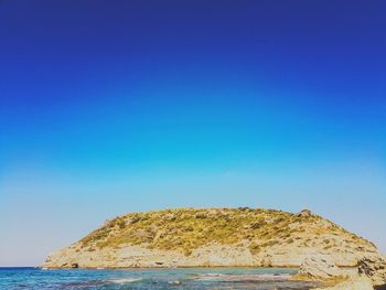 Rock formations by sea against clear blue sky