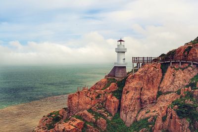 Lighthouse by sea against cloudy sky