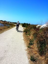 Man riding bicycle on road against clear sky