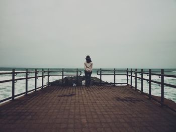 Rear view of man standing on railing against sea