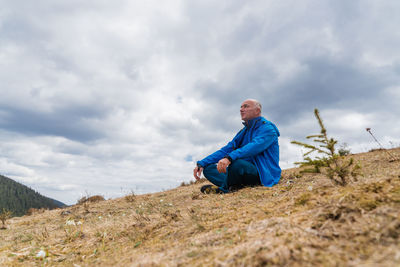 Side view of man sitting on field against sky