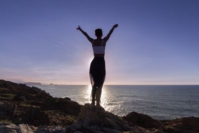 Woman with arms raised standing at beach against sky