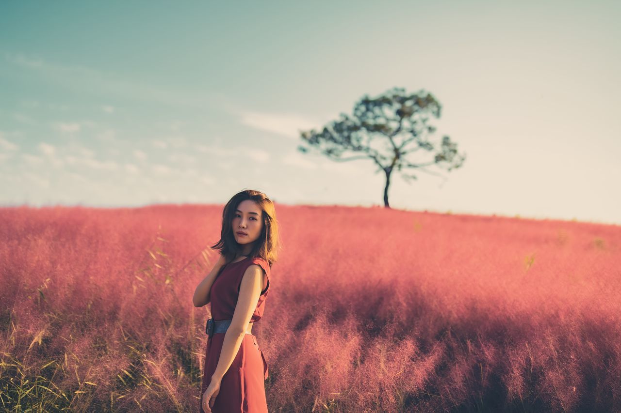 field, land, one person, sky, plant, standing, lifestyles, real people, young adult, leisure activity, young women, women, nature, beauty, looking at camera, portrait, beautiful woman, adult, environment, fashion, outdoors, hairstyle