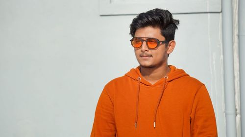 Young man in hoodie looking away standing against wall outdoors