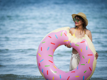 Portrait of woman holding donut pattern inflatable ring at beach