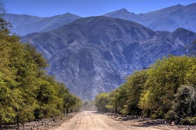 Road amidst trees and mountains against sky