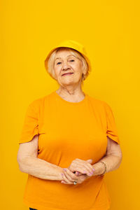 Portrait of young woman with arms crossed against yellow background