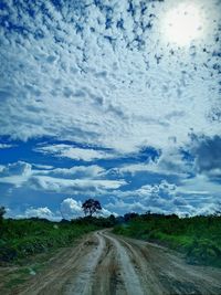 Dirt road amidst field against sky