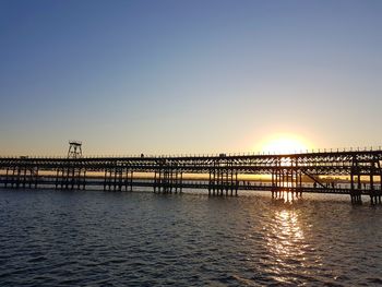 Pier over sea against clear sky during sunset