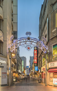 Illuminated street amidst buildings against sky in city