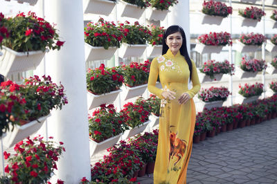 Portrait of smiling young woman standing by flower pot