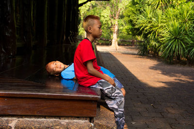 Boy sitting on bench against trees