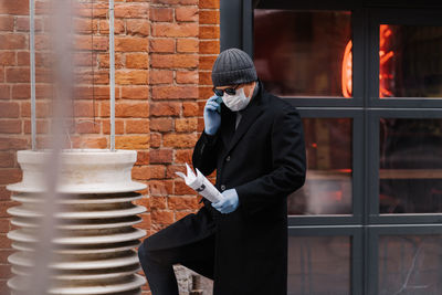 Full length of man holding camera while standing against brick wall