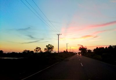 Road by silhouette trees against sky during sunset