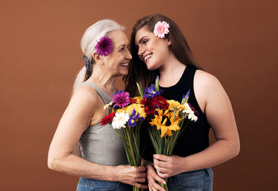 Beautiful young woman holding flower bouquet against orange background