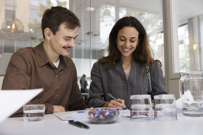 Man looking at smiling woman signing agreement at desk in real estate office